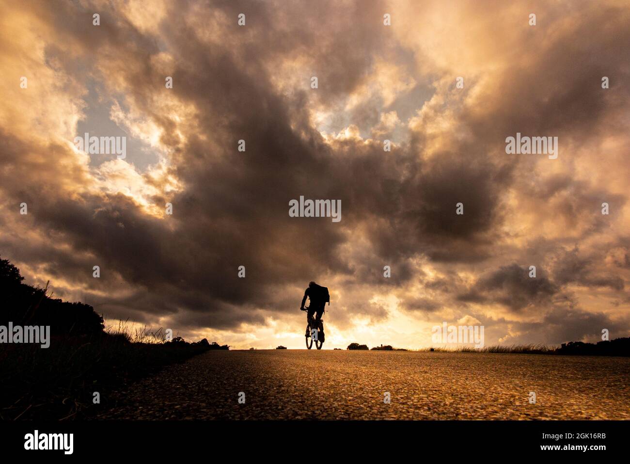 Cieli spettacolari mentre il sole tramonta a Richmond Park e un ciclista si dirige a casa Foto Stock