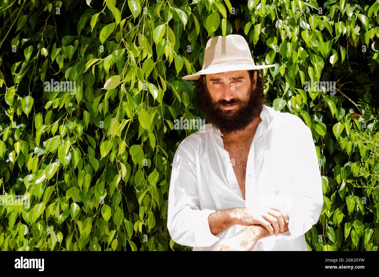 il giovane uomo con barba e capelli lunghi indossa cappello e camicia  bianca circondata dal verde Foto stock - Alamy