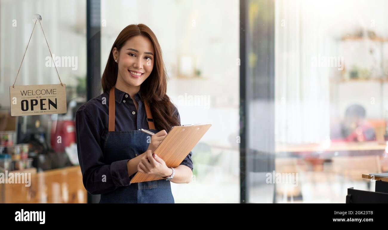 Ritratto di un imprenditore asiatico sorridente in piedi dietro il suo bancone caffè con cartello aperto Foto Stock