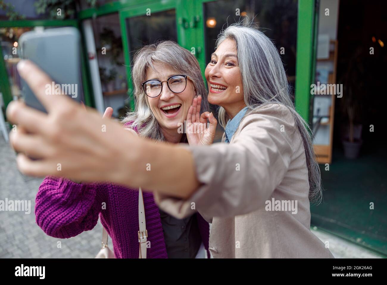 Positiva Senior Asian signora con capelli grigio amico prendere selfie sulla strada moderna della città Foto Stock