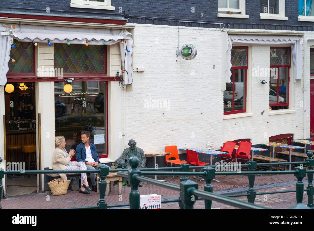 Amsterdam Paesi Bassi - Agosto 20 2017; coppia seduta accanto al bronzo statuto fuori Festina Lente caffè chiacchierando e gustando caffè sulla strada. Foto Stock