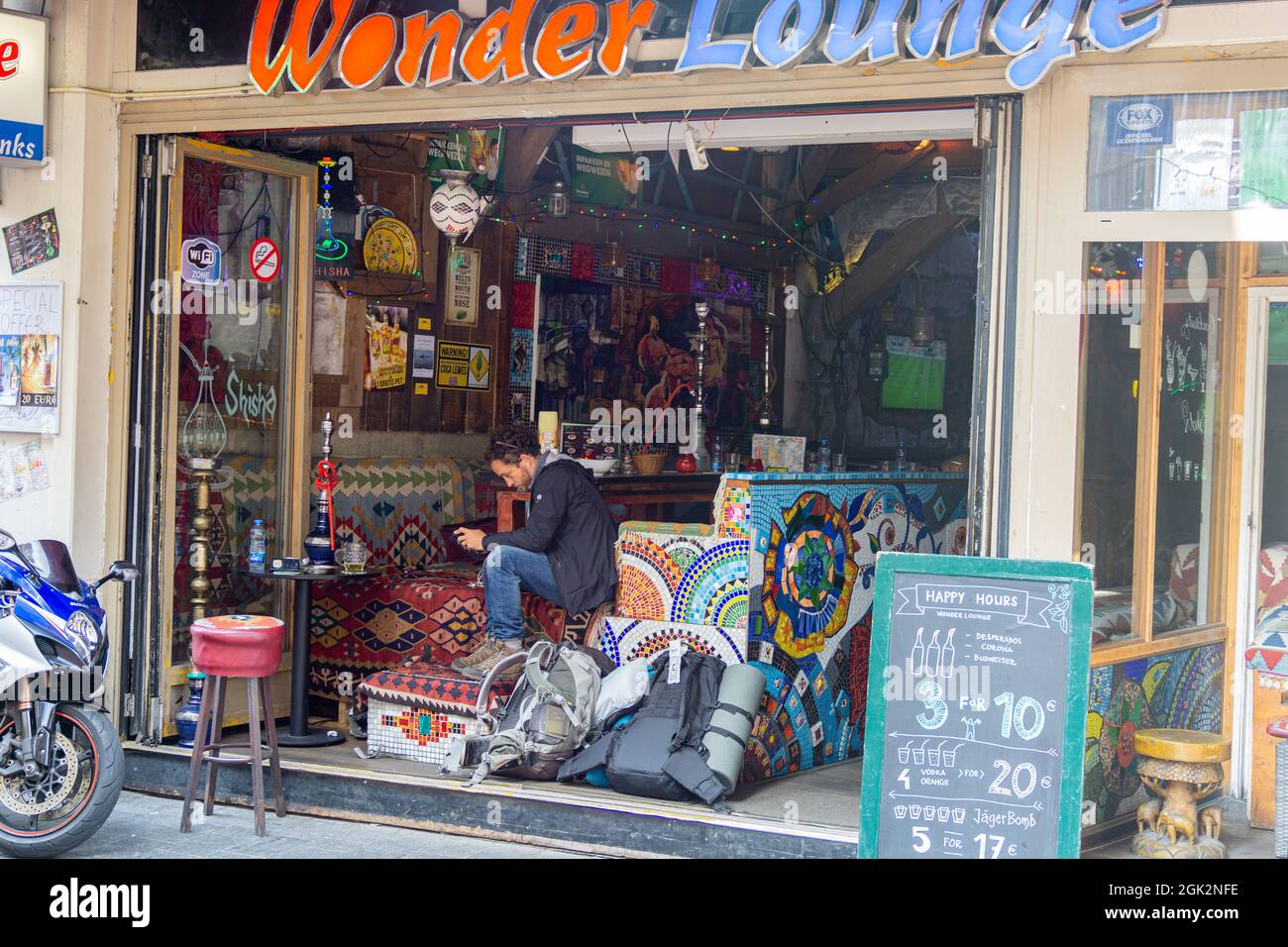 Amsterdam-Netherlands - Agosto 21 2017; l'uomo siede a controllare il suo cellulare all'ingresso di un caffe' cittadino dai colori bizzarri con pannelli a mosaico e backpa Foto Stock