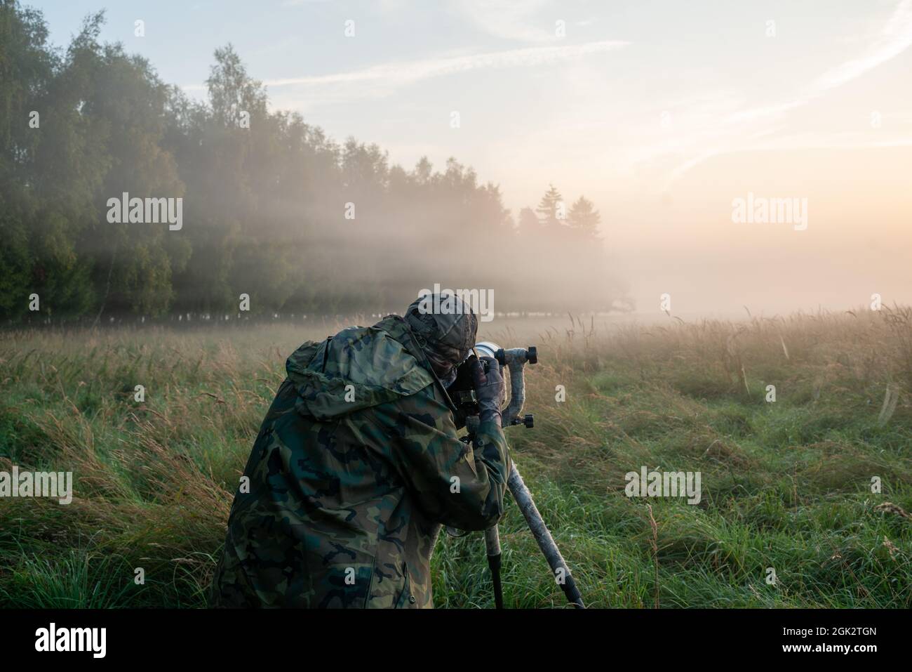 Fotografo della natura in piedi in abiti camuffati con una macchina fotografica su un cavalletto Foto Stock