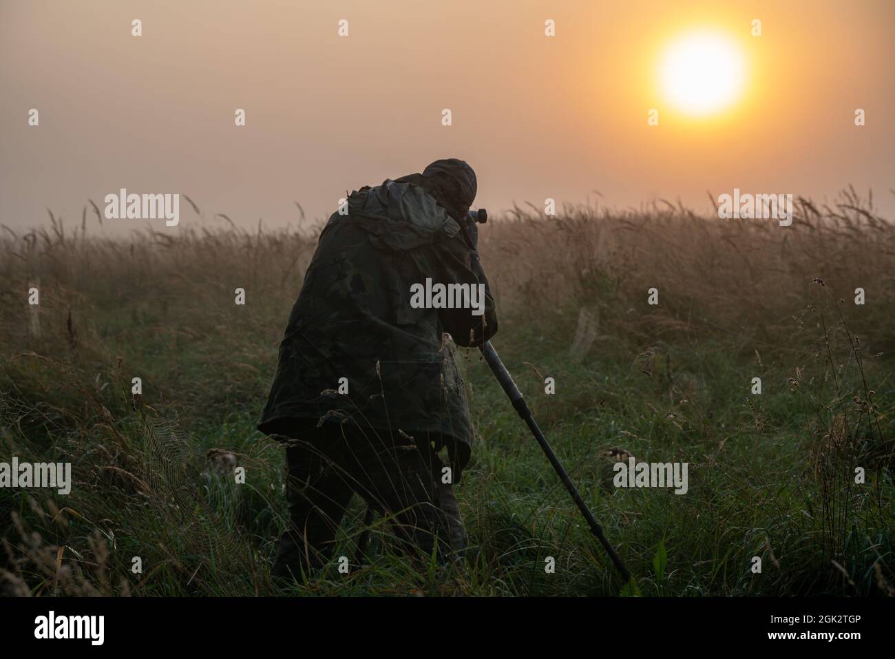 Fotografo della natura in piedi in abiti camuffati con una macchina fotografica su un cavalletto Foto Stock