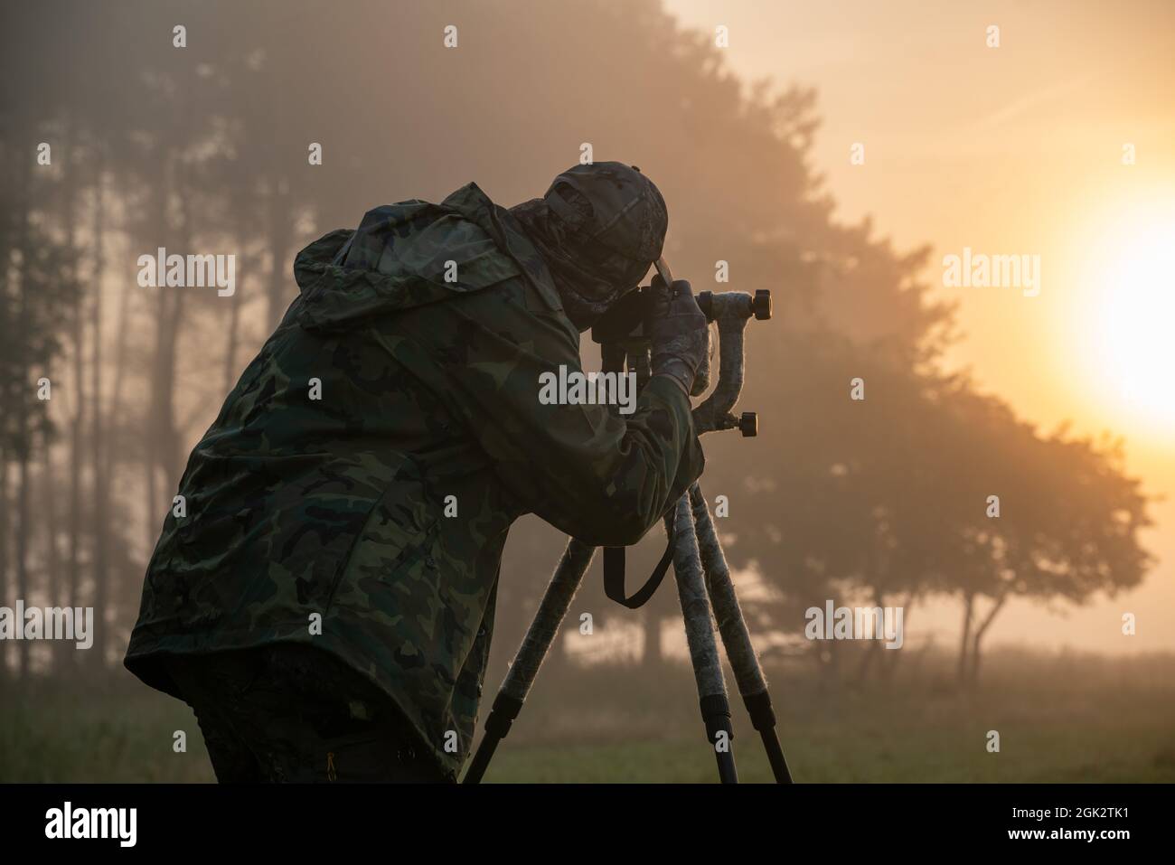 Fotografo della natura in piedi in abiti camuffati con una macchina fotografica su un cavalletto Foto Stock