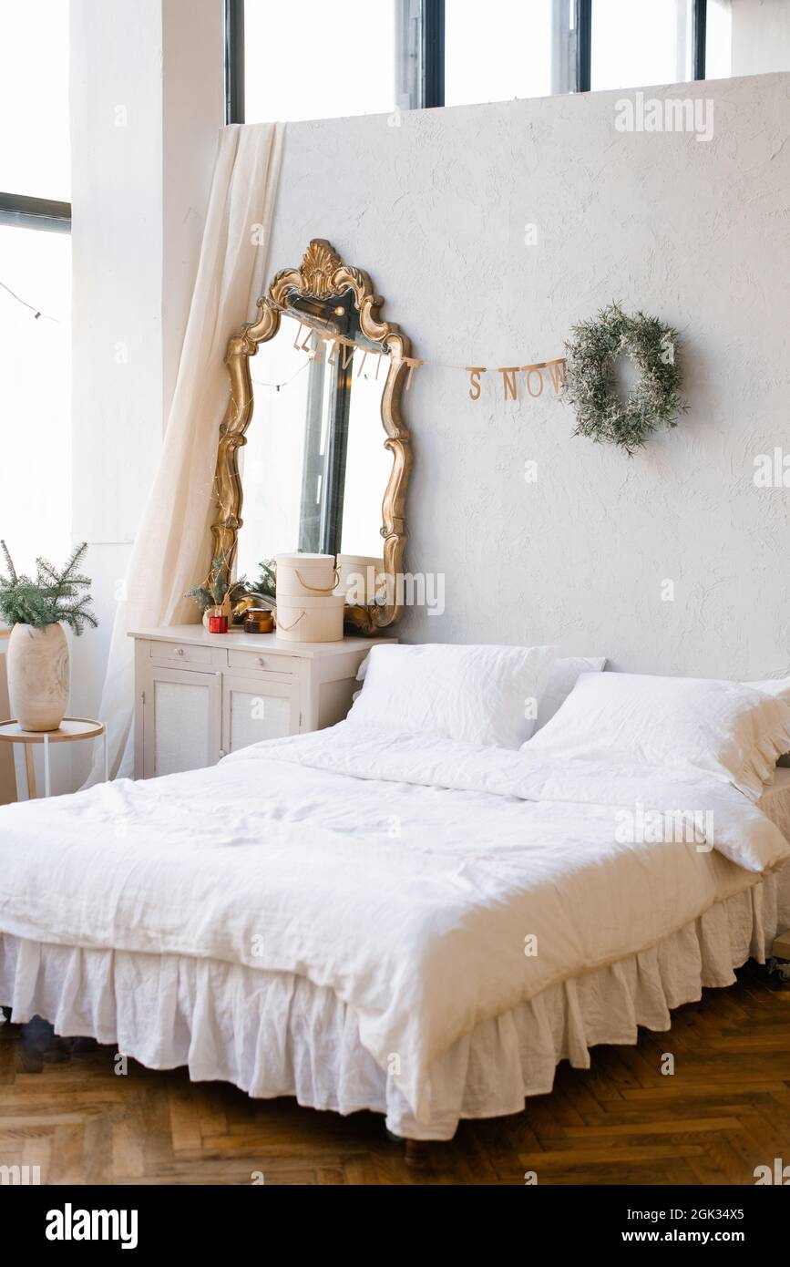 Un letto matrimoniale con lenzuola bianche e cuscini nella camera da letto  decorata per Natale e Capodanno. Corona di Natale vicino allo specchio  presso il comò Foto stock - Alamy