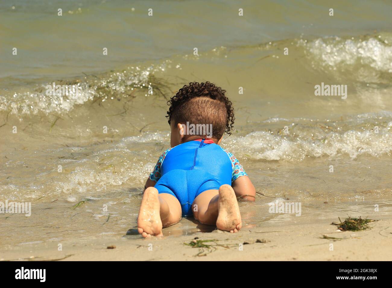 Carino bambino africano con capelli ricci adagiato su una spiaggia Foto Stock