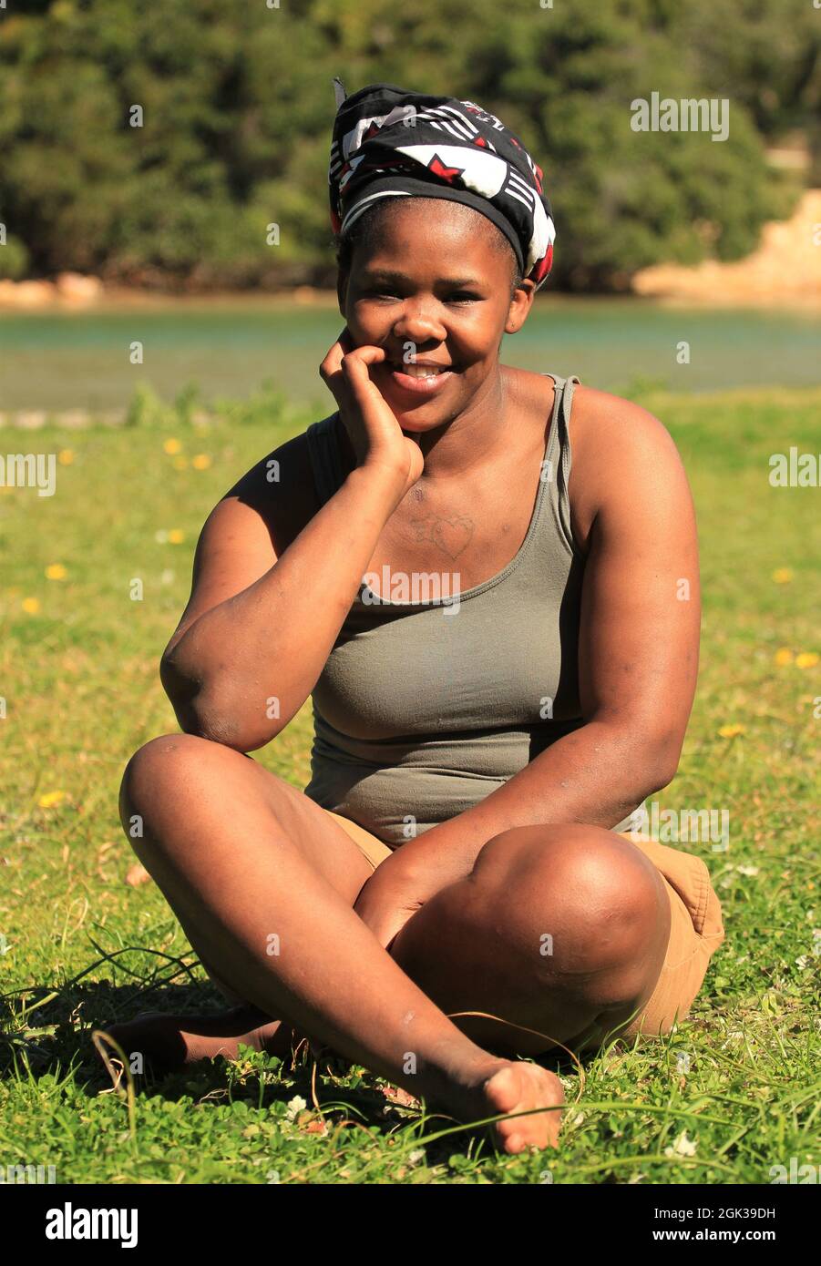 Yopung ragazza nera con sorriso amichevole seduto su un prato Foto Stock
