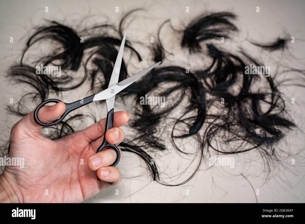 Forbici professionali per il taglio dei capelli nella mano sinistra con i capelli sul pavimento Foto Stock