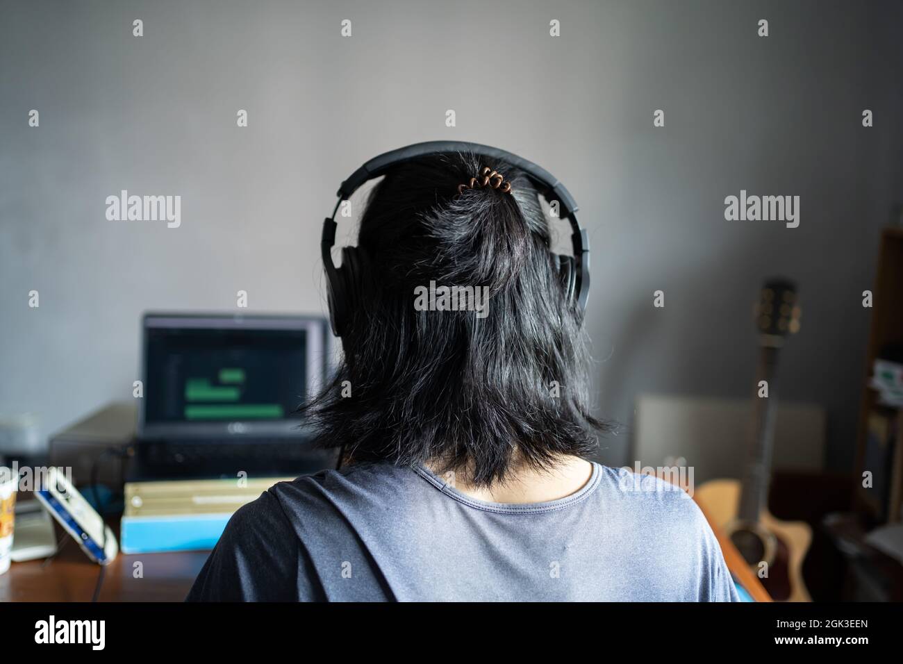 Uomo con capelli lunghi che indossa le cuffie e che siede di fronte al computer portatile. Musicista che lavora da casa. Foto Stock