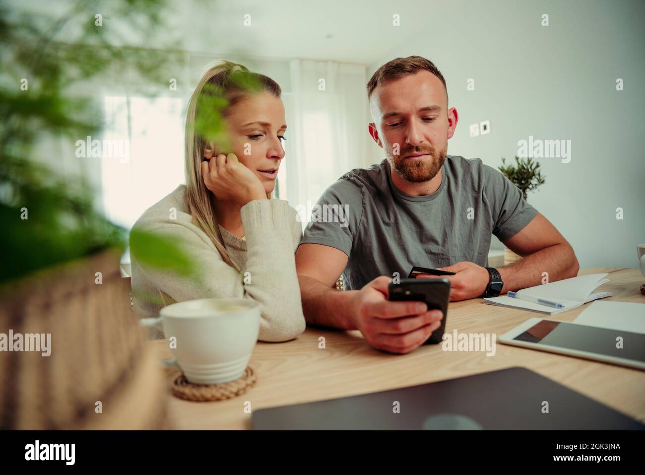 Coppia caucasica seduta a casa al tavolo da cucina digitando su dispositivo cellulare Foto Stock