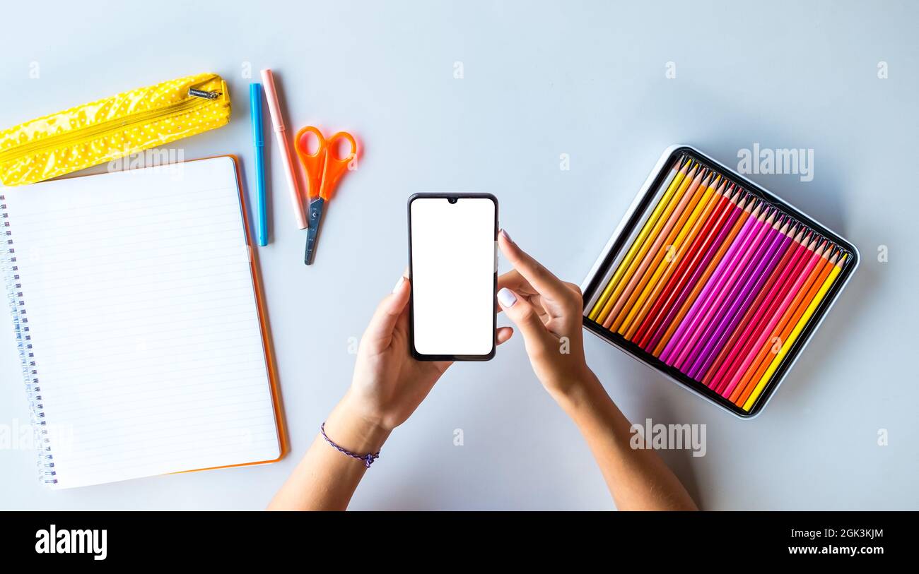 Smartphone torna a scuola schermo vuoto con mani adolescenti e matite colorate. Personalizzazione per pubblicità, siti Web e applicazioni. Foto Stock