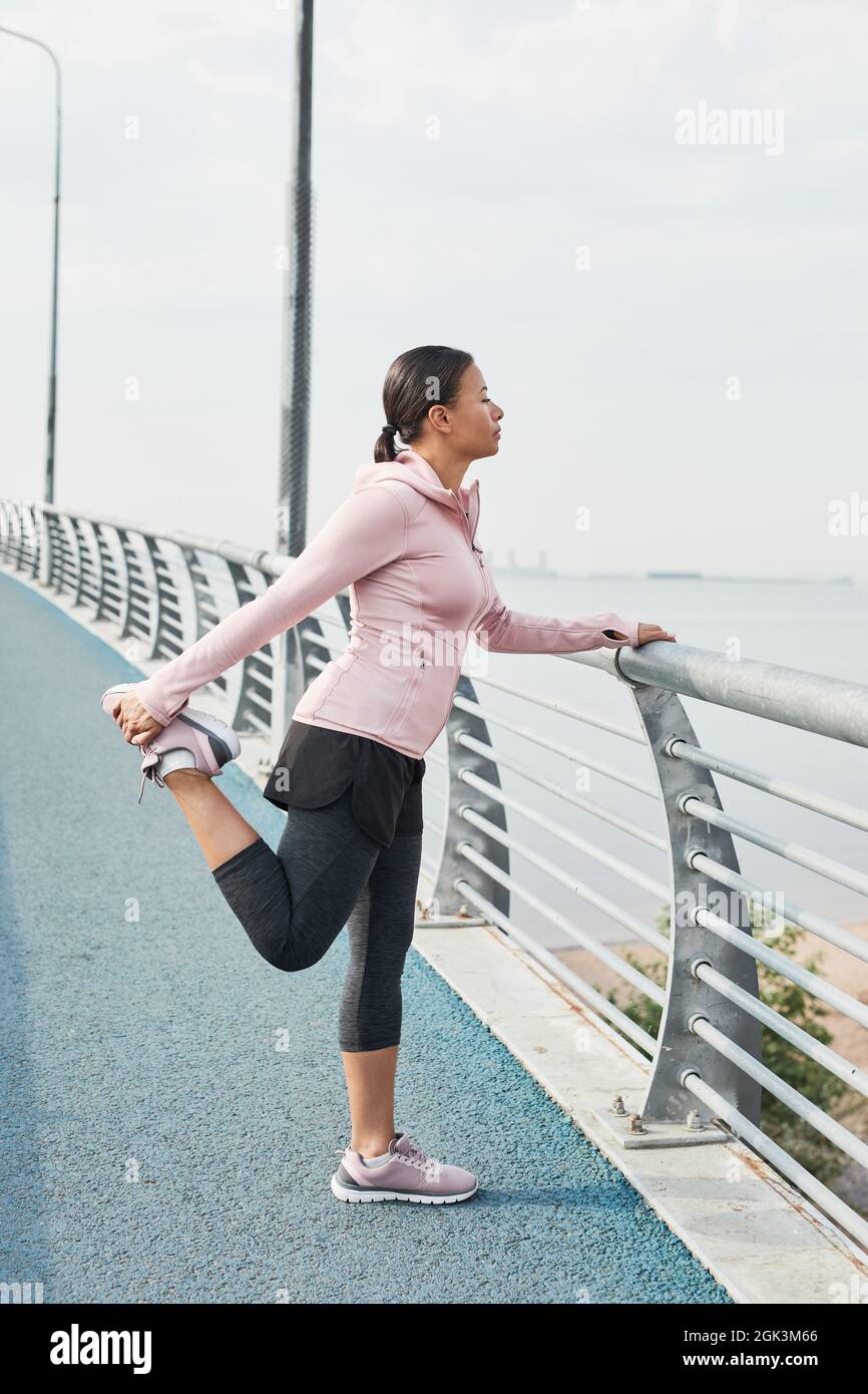 Giovane donna in abbigliamento sportivo in piedi sul ponte facendo esercizio e guardando il mare bello Foto Stock
