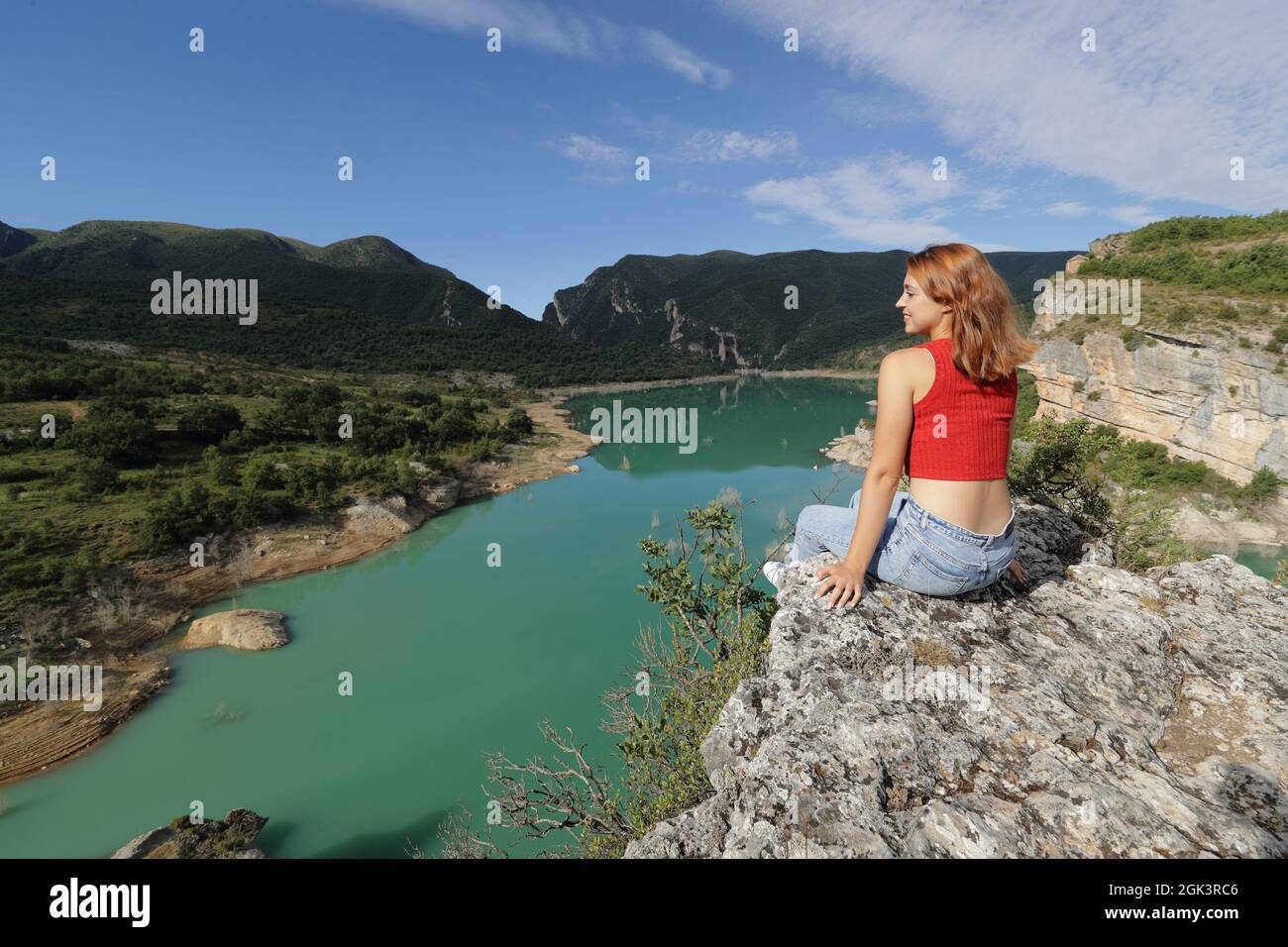 Donna felice in rosso che contempla la vista di un lago in cima a una scogliera in montagna Foto Stock