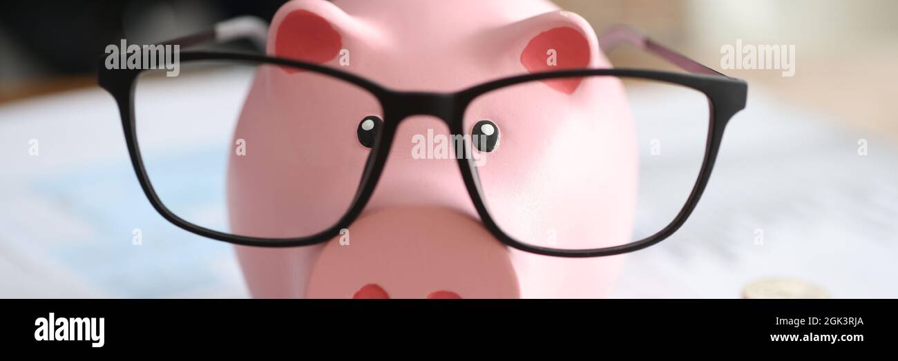 Porcellino rosa banca in occhiali vicino a business grafici e. monete Foto Stock