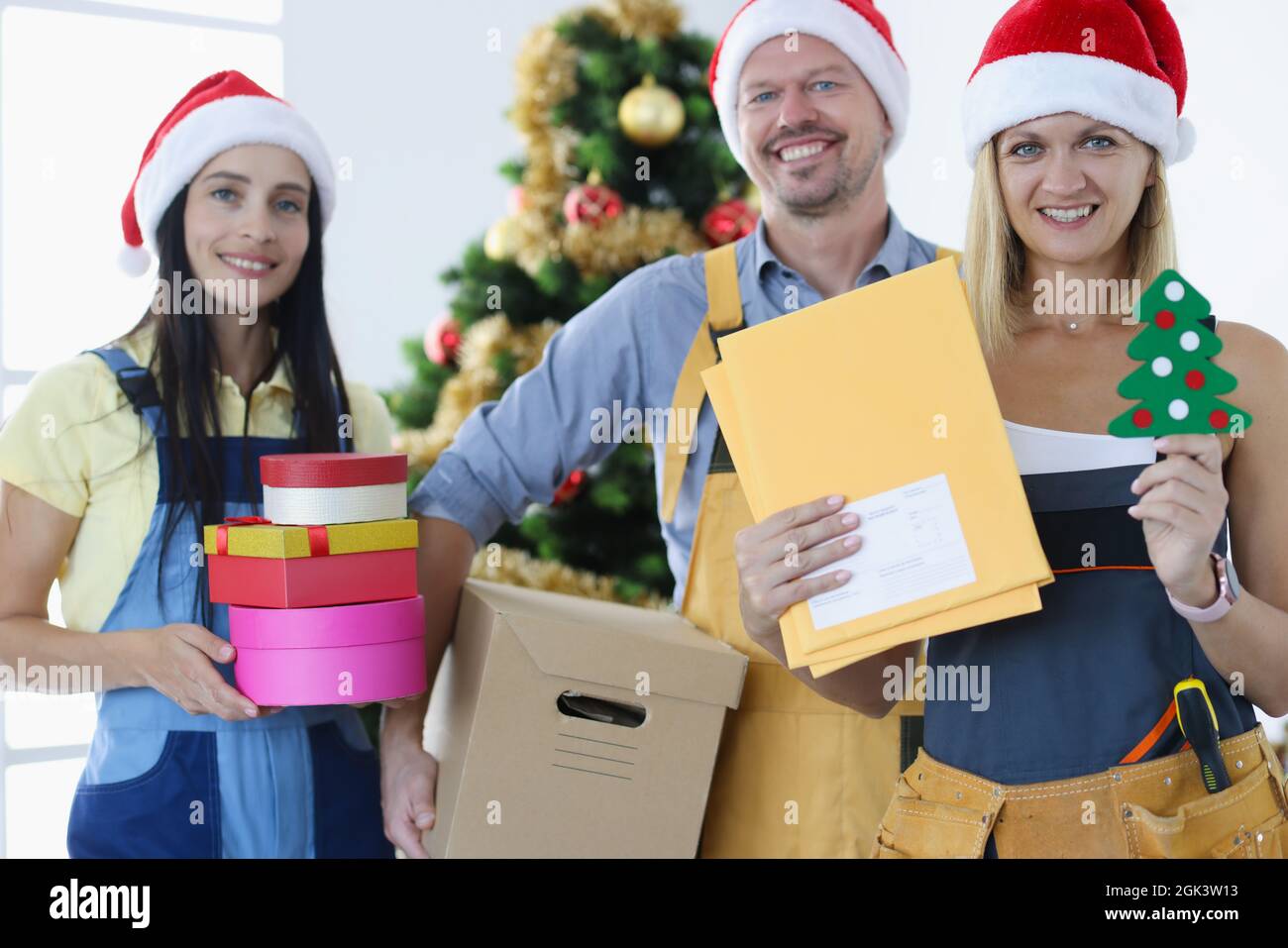 Gruppo di corrieri in cappelli babbo natale in piedi vicino albero di natale e tenendo molte scatole regalo Foto Stock