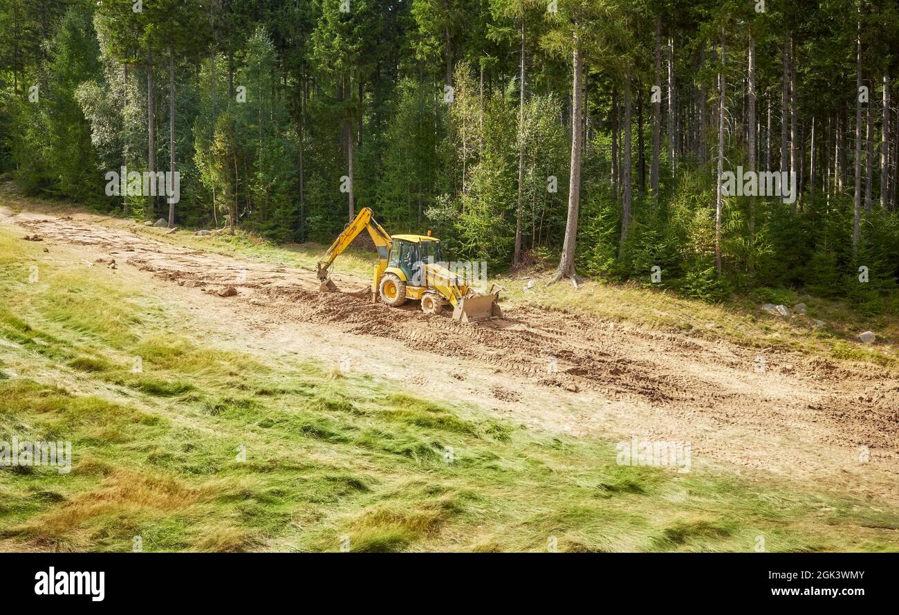 Il retroescavatore livella la superficie della collina per una pista da sci. Foto Stock