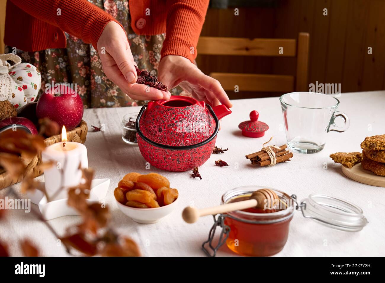 Accoglienti giornate autunnali. Donna che indossa un maglione arancione, prepara il tè in teiera rossa sul tavolo con tovaglia di lino. Umore aromatico. Vibrazioni autunnali. Tè bevendo. Che Foto Stock