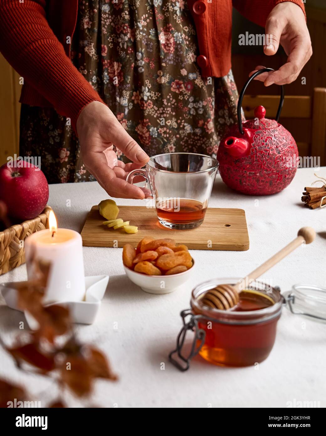 Accoglienti giornate autunnali. Donna che indossa un maglione arancione, prepara il tè in teiera rossa sul tavolo con tovaglia di lino. Umore aromatico. Vibrazioni autunnali. Tè bevendo. Che Foto Stock