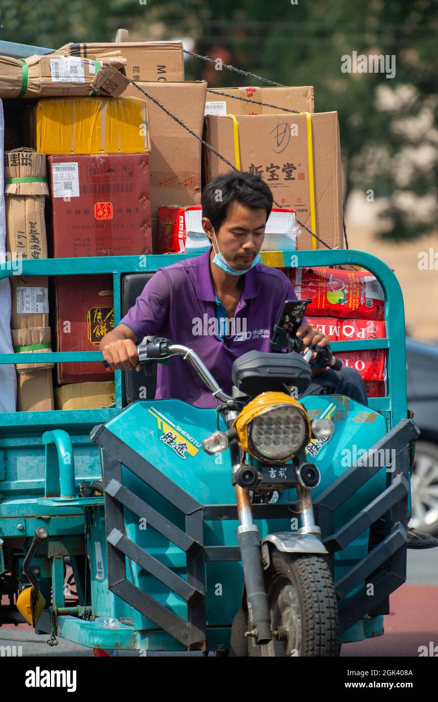 Un corriere cinese controlla il suo telefono cellulare mentre consegna le merci con uno scooter elettrico a Pechino, Cina. 13 settembre 2021 Foto Stock