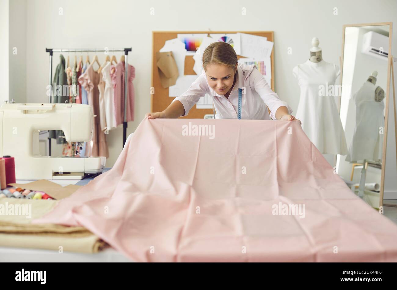 Donna felice che guadagna una vita come un dressmaker che lavora con il tessuto nel suo studio Foto Stock
