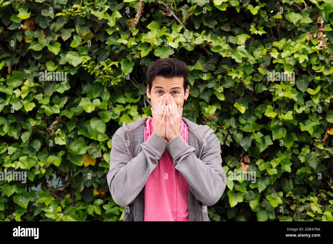 sorpreso adolescente che copre la sua bocca con le mani su uno sfondo verde piante, concetto di espressioni e emozioni umane, copia spazio per il testo Foto Stock