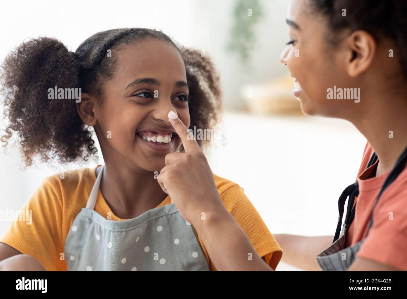 Primo piano di donna nera macchiando il naso della figlia con farina Foto Stock