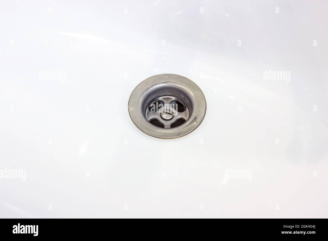 Foro di scarico dell'acqua metallico nel lavello in ceramica bianca nel bagno in primo piano. Foto Stock