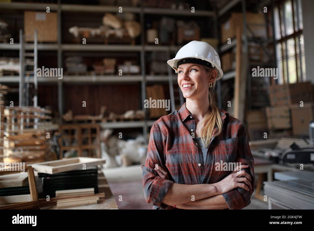 Ritratto di carpentiere femminile di metà-adulto in piedi in officina di carpenteria, guardando da parte e sorridente. Concetto di piccola impresa. Foto Stock