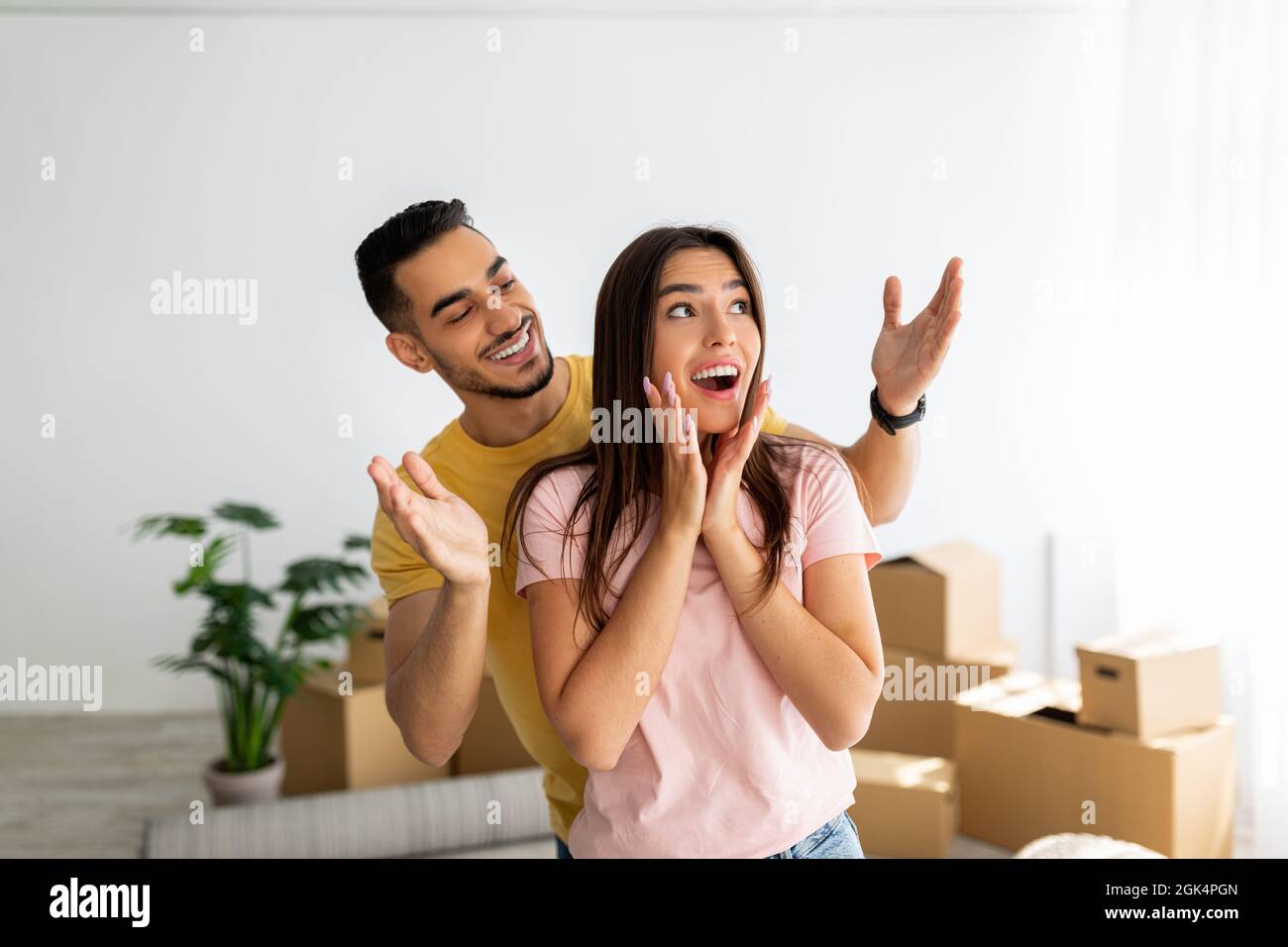Eccitato ragazzo arabo sorprende la sua ragazza caucasica, che si sposta a casa propria insieme, in piedi in casa tra le scatole Foto Stock