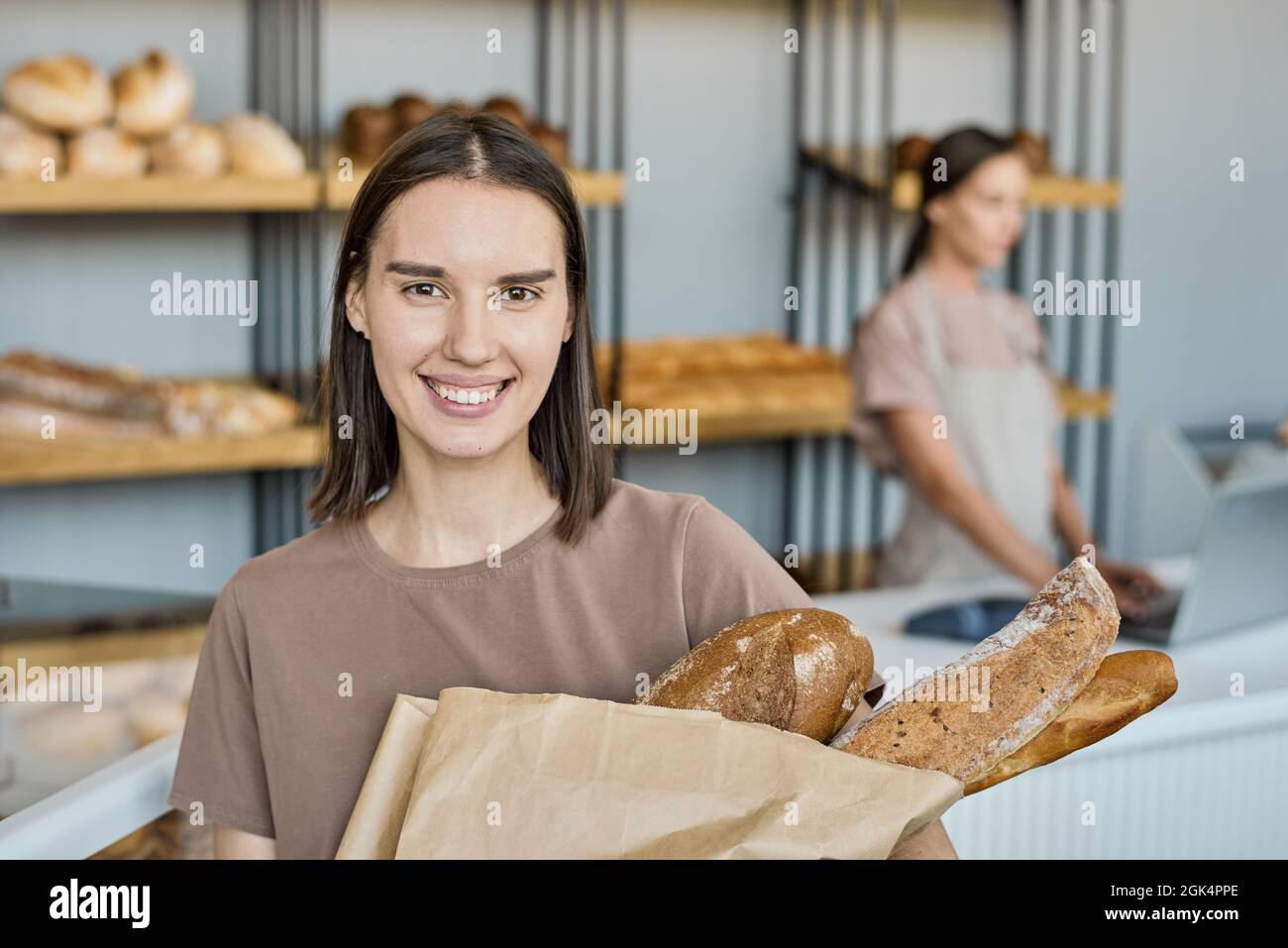 Ritratto di sorridente giovane cliente che tiene fresco pane cotto in sacchetto con l'aperbag contro stalla Foto Stock