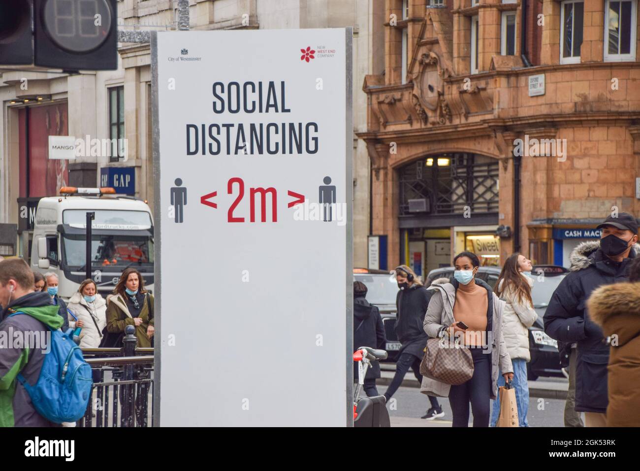 Le persone che indossano maschere protettive passeggiano davanti a un segno sociale di allontanamento su Oxford Circus durante la pandemia del coronavirus. Londra, Regno Unito 2 dicembre 2020. Foto Stock