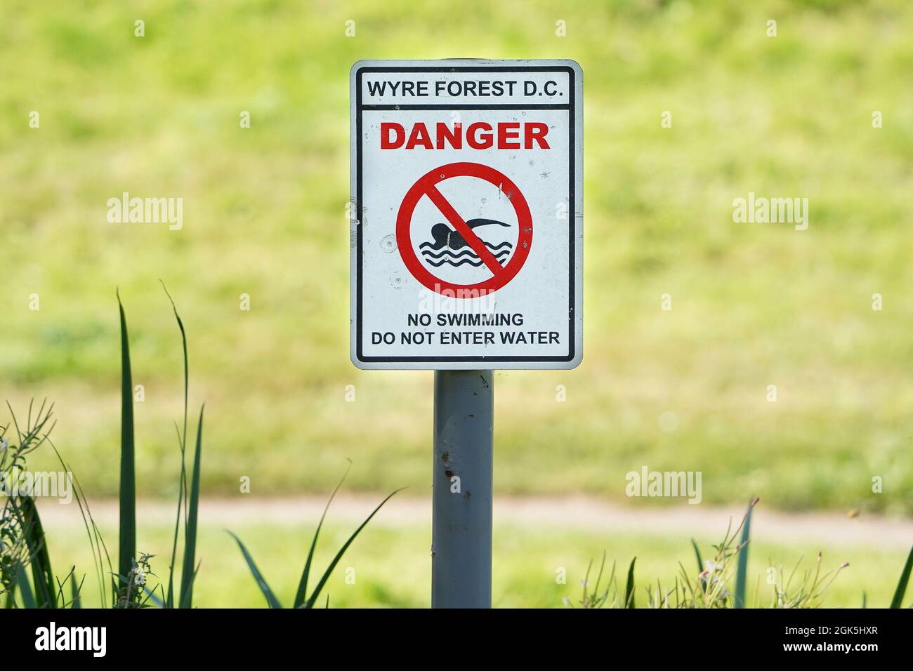 Primo piano del cartello di sicurezza del consiglio sul lato dell'acqua del canale di campagna: "Pericolo, divieto di nuoto, non entrare in acqua". Foto Stock