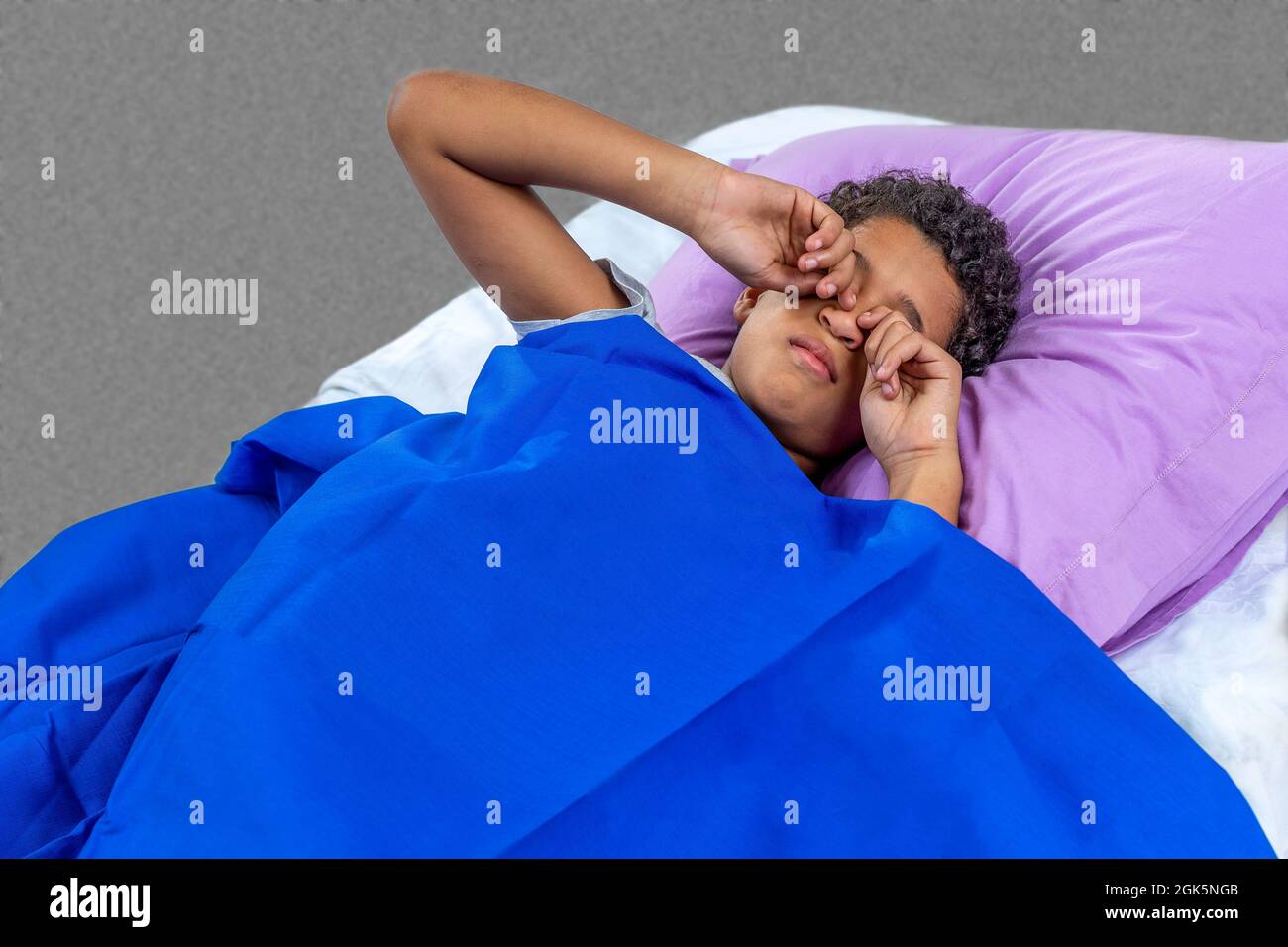 Primo piano sul ragazzo singolo sfregando gli occhi con entrambe le mani mentre è a letto per dormire Foto Stock