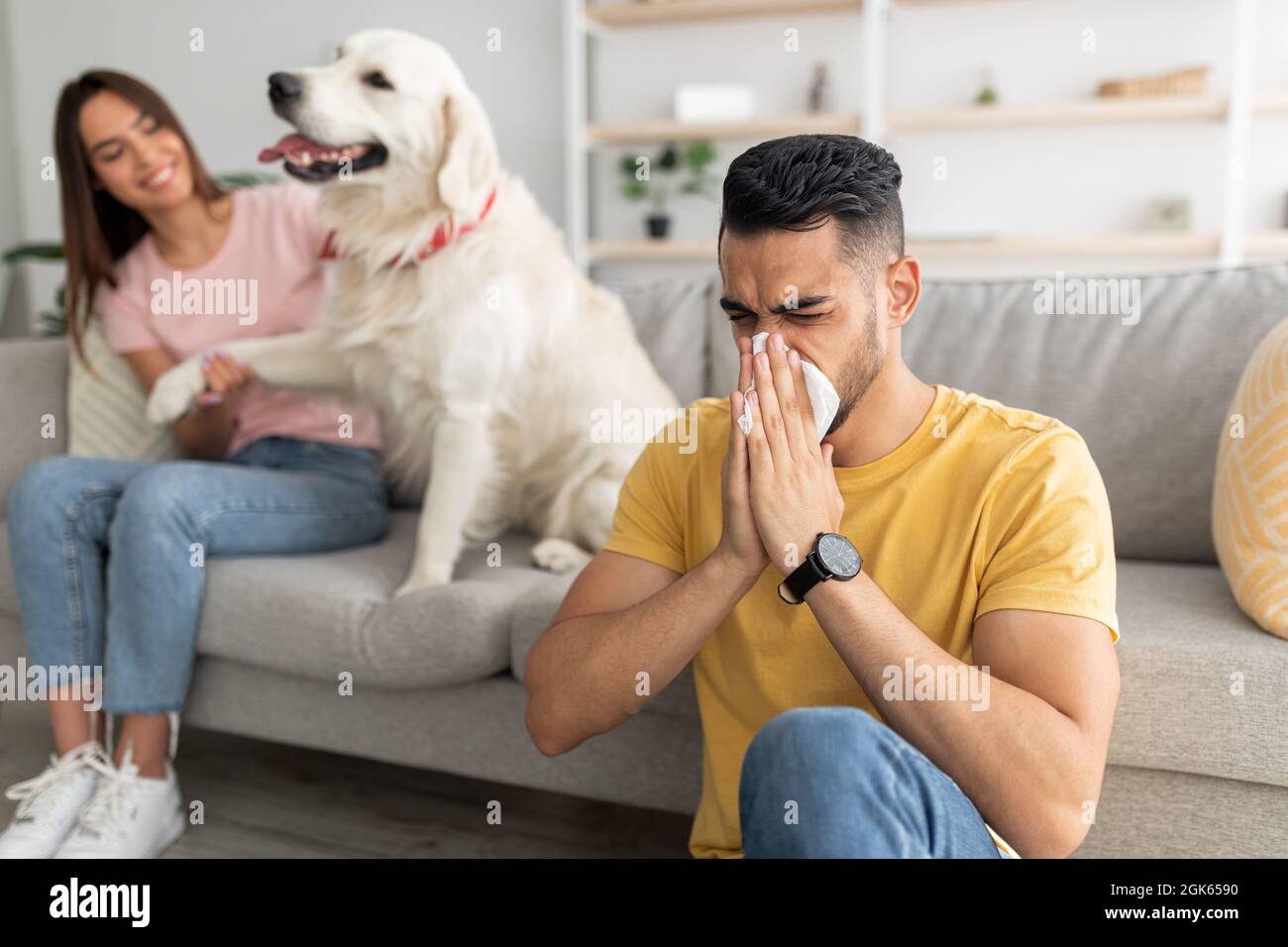 Malato arabo ragazzo che ha freddo, soffia naso, starnuti in carta tissue, la sua ragazza con cane da compagnia su sfondo, copia spazio Foto Stock