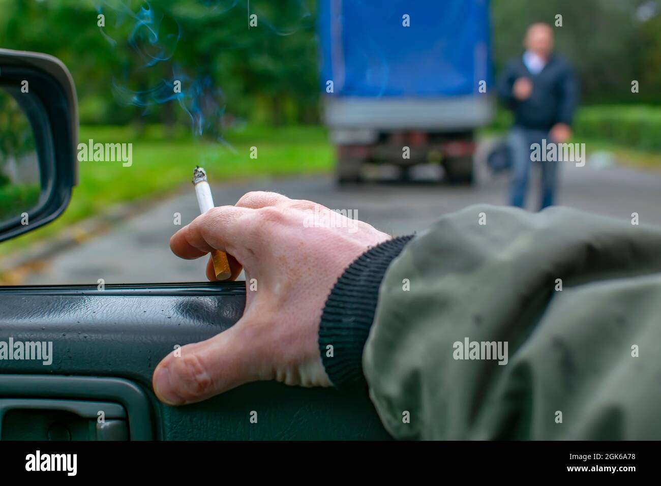 mano di un uomo, di un conducente, di un fumatore che è seduto in un'auto, tenendo una sigaretta fumante Foto Stock