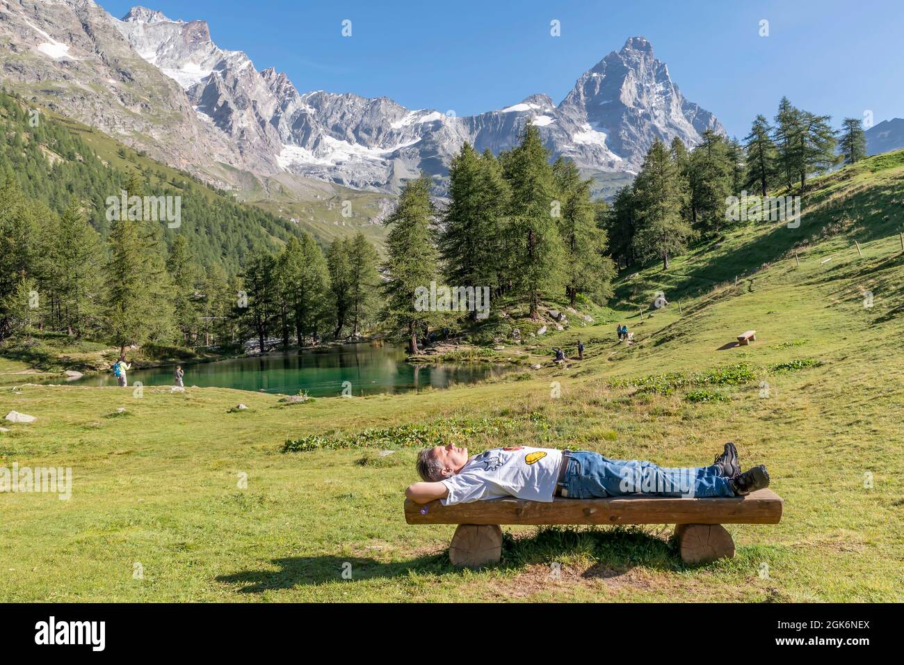 Un uomo bianco sdraiato al sole su una panchina di legno godendo della tranquillità del Lago Blu, Valle d'Aosta, Italia Foto Stock
