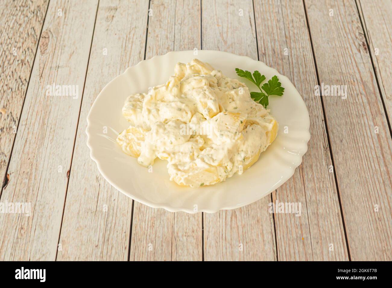 Tipica tapa spagnola di patate cotte con salsa aioli in un piatto bianco su sfondo di strisce di legno bianco Foto Stock