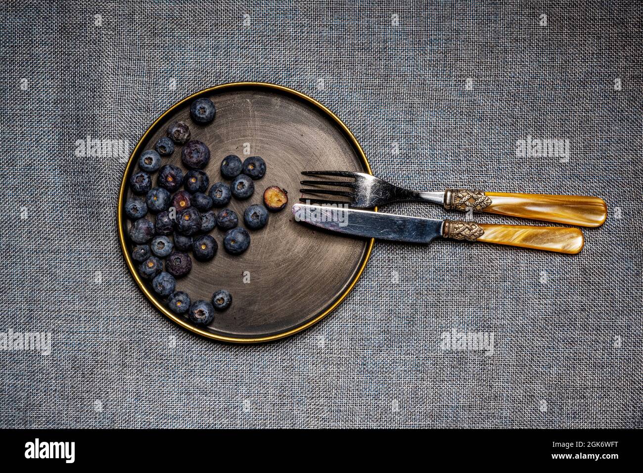Piatto con coltello vintage e forchetta piena di mirtilli su panno grigio Foto Stock