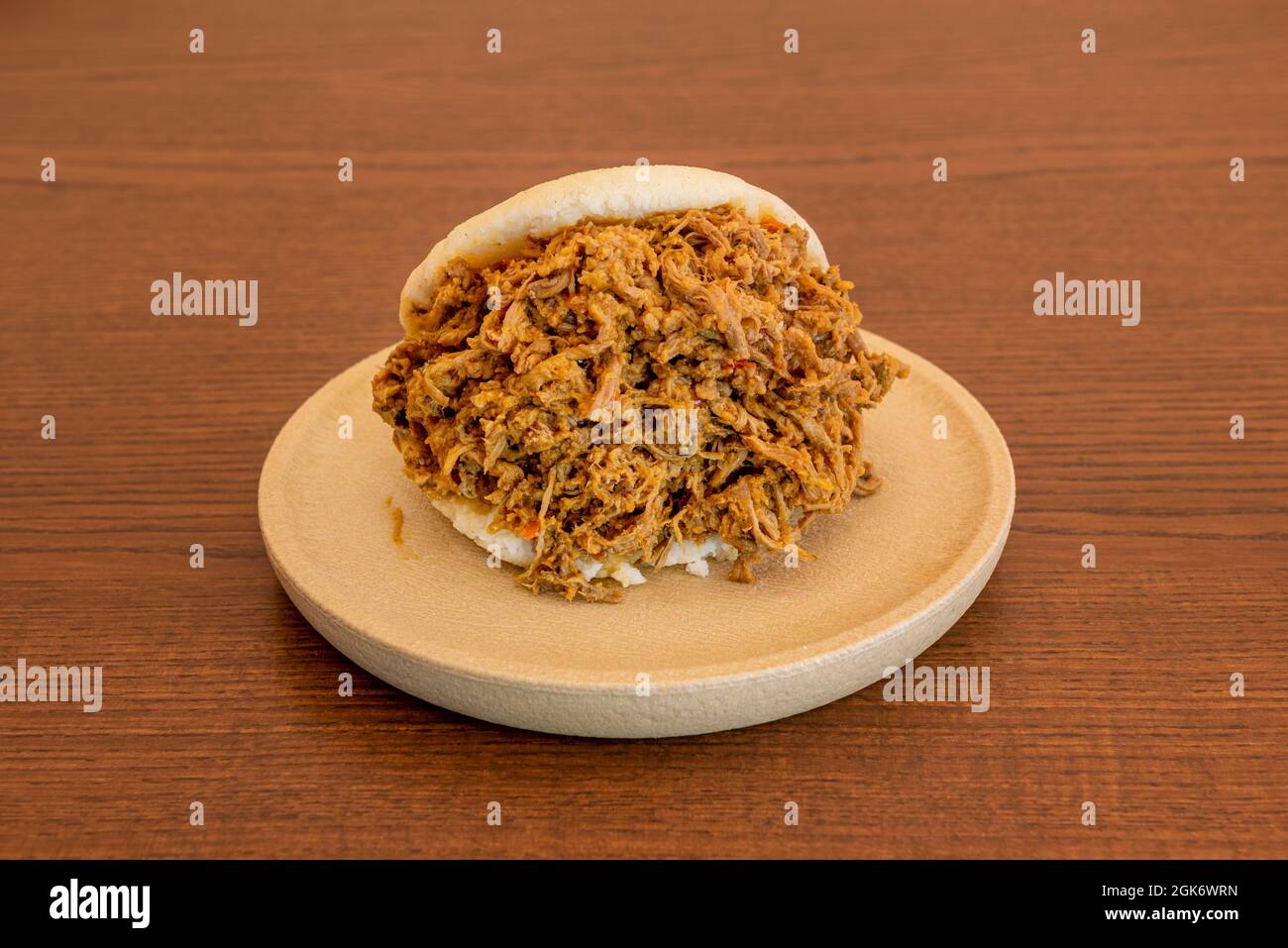 Arepa traboccante di carne grattugiata con una classica ricetta venezuelana su un piatto rotondo in resina e tavolo in legno Foto Stock