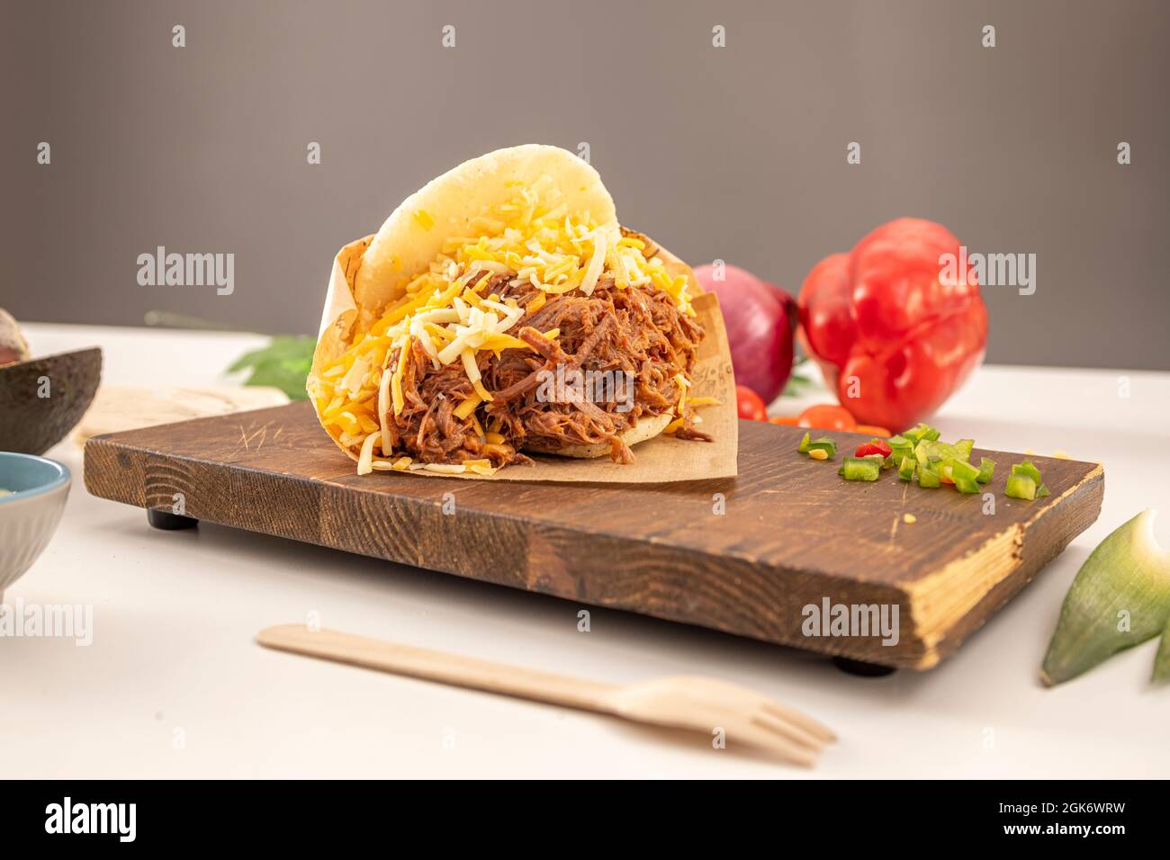 Arepa di manzo grattugiata venezuelana con formaggio grattugiato di vari sapori con avocado, peperoni e cipolle, su vassoio di legno Foto Stock