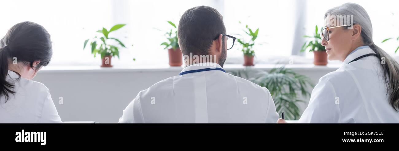 vista posteriore dei giovani medici vicino all'età media collega asiatico in sala riunioni, banner Foto Stock