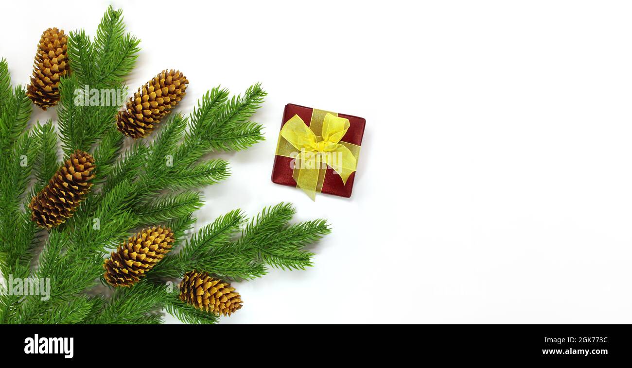Rami di abete con coni nell'angolo e scatola regalo rossa con arco giallo su sfondo bianco. Natale, Capodanno. Spazio di copia Foto Stock