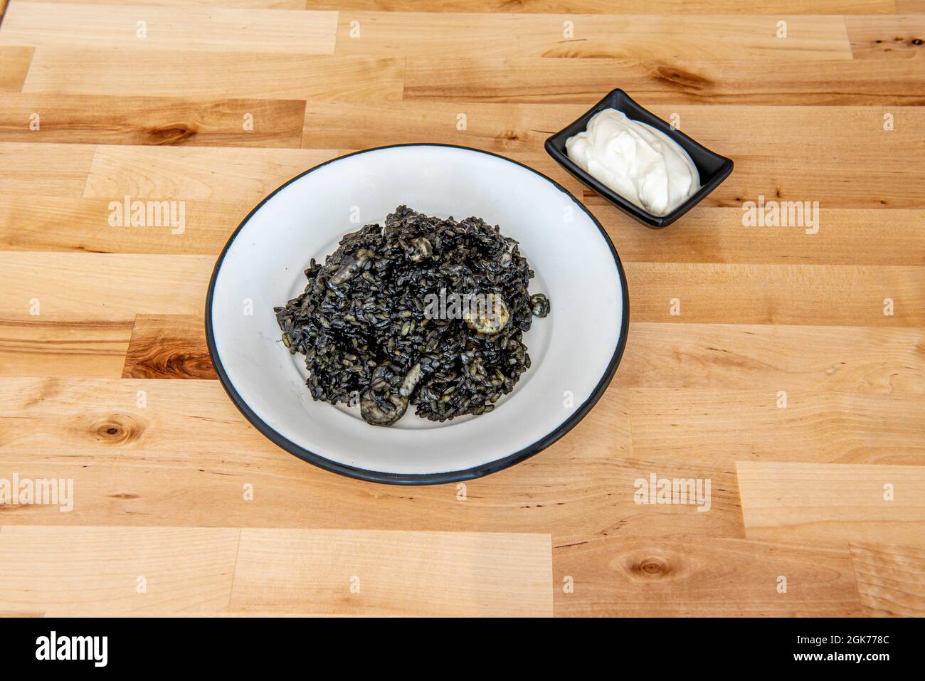 Porzione di paella nera spagnola con salsa aioli da servire come tapas su tavola di legno Foto Stock