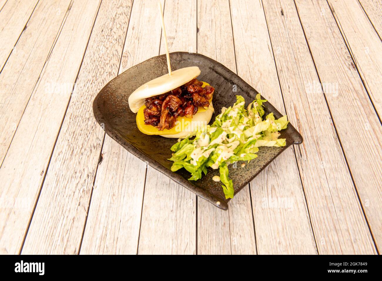 Panino Bao con pollo teriyaki e insalata di lattuga su tavola bianca Foto Stock