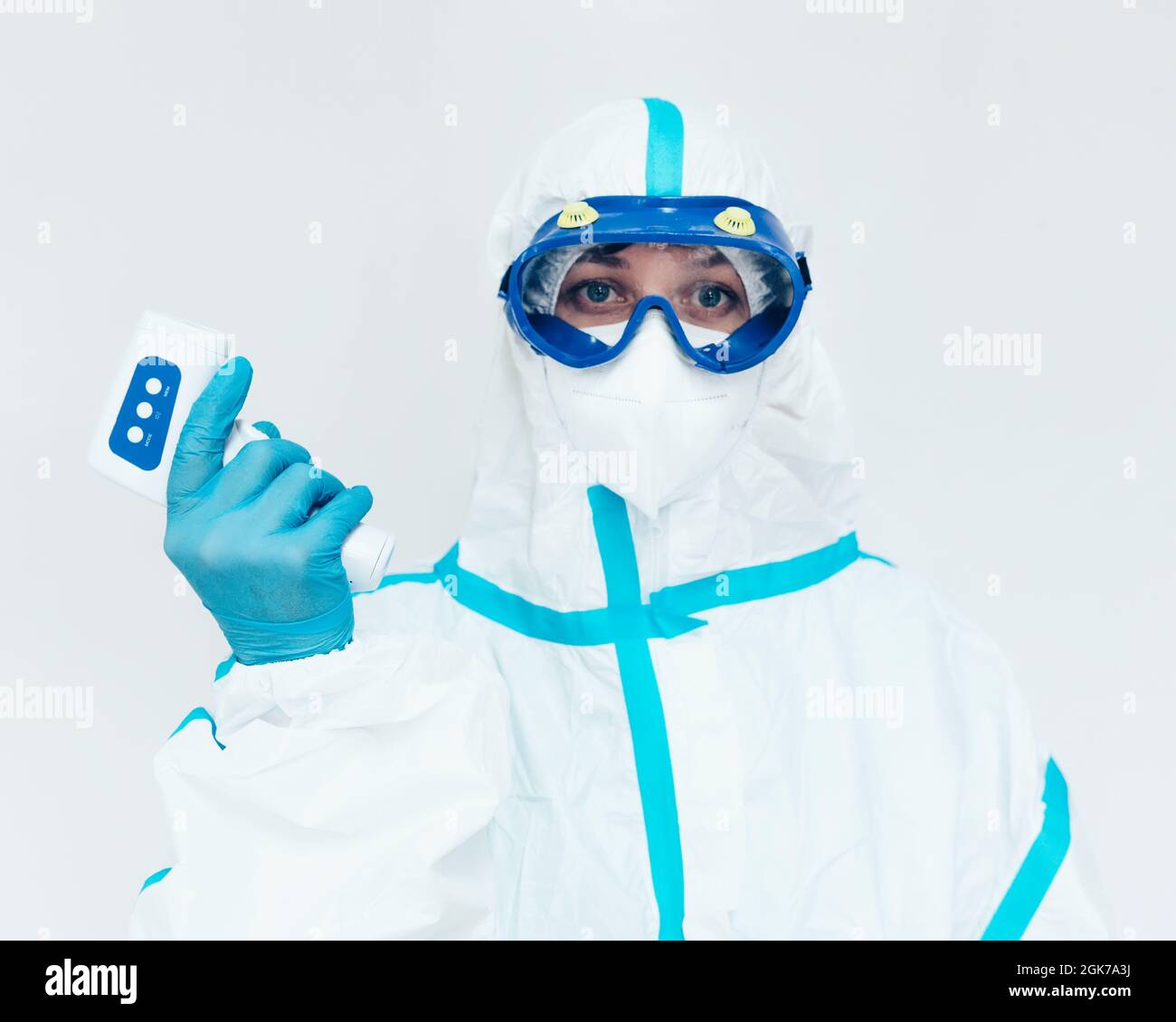 Un medico in un vestito medico protettivo e maschera tiene un termometro a infrarossi moderno in mano. Misurazione della temperatura corporea con un termometro senza contatto. Controllo della malattia di Covid-19. Foto Stock