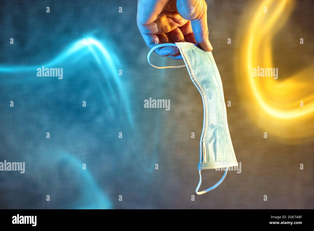 Maschera medica per il viso tenuta da una mano con effetti di luce colorati Foto Stock