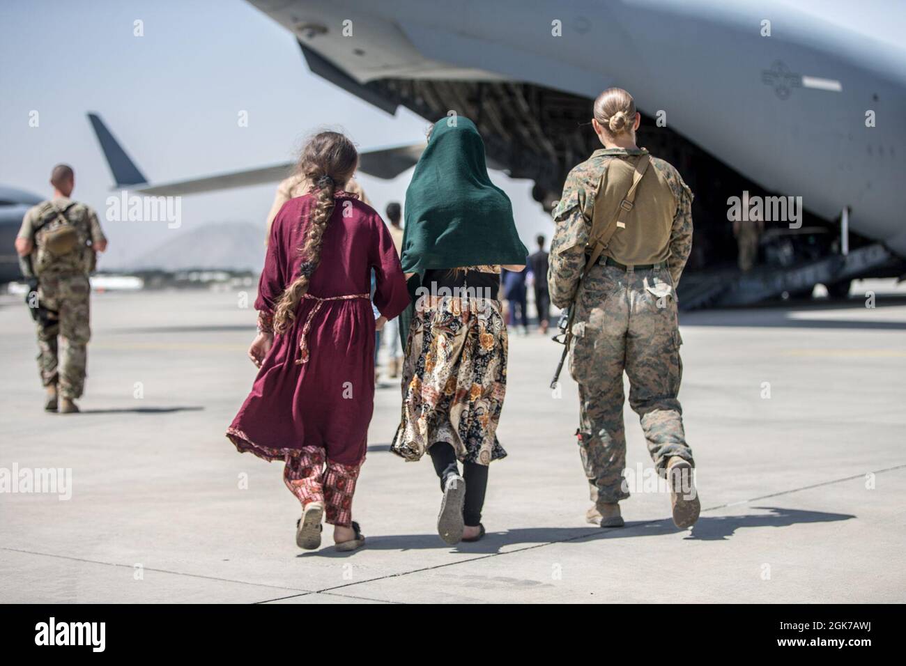 Una Marina con la 24a unità di spedizione Marina (MEU) cammina con i bambini durante un'evacuazione all'Aeroporto Internazionale Hamid Karzai, Kabul, Afghanistan, 24 agosto. I membri del servizio degli Stati Uniti stanno assistendo il Dipartimento di Stato con un prelievo ordinato di personale designato in Afghanistan. Foto Stock