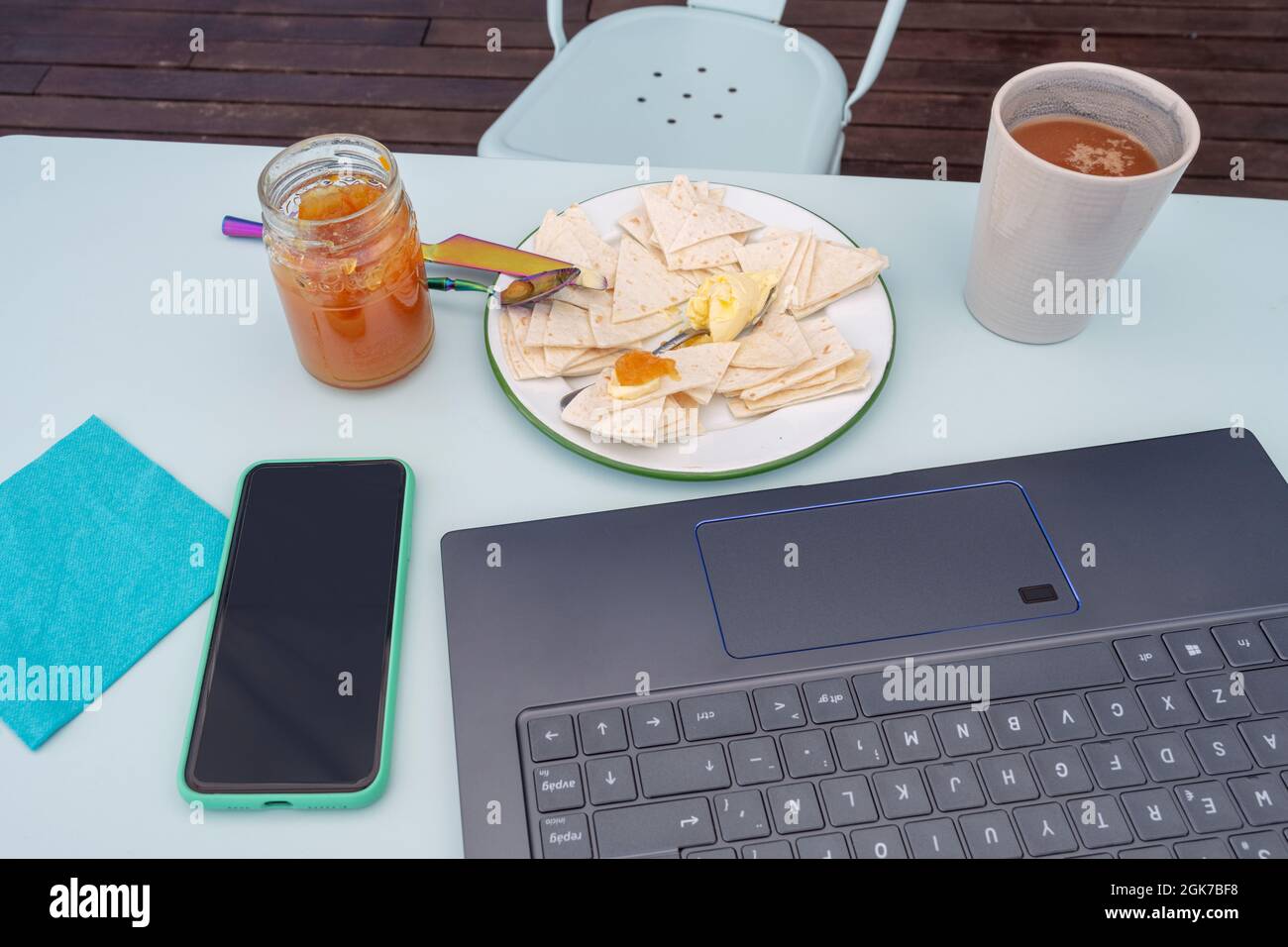 Telelavoro e fare colazione davanti al pc con caffè con latte e pane con burro e marmellata d'arancia amara Foto Stock