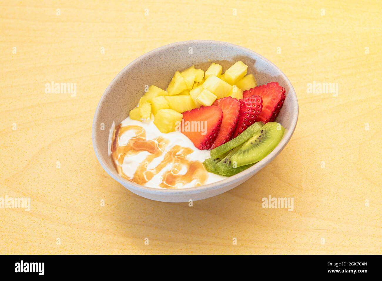 Ciotola di frutta fresca con yogurt e sciroppo. Ananas, kiwi e fragole tritate su tavola gialla Foto Stock